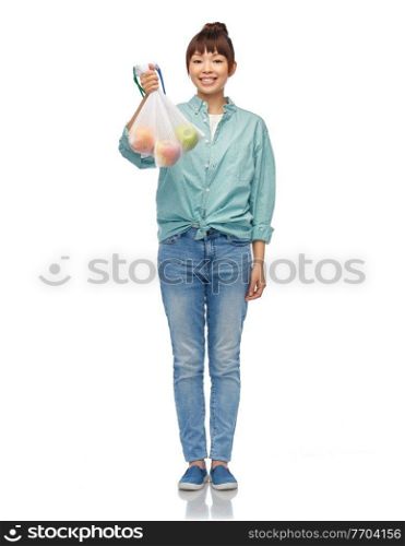 sustainability, eco living and people concept - portrait of happy smiling young asian woman in turquoise shirt and jeans holding reusable net bag with apples over white background. happy woman with apples in reusable net bag
