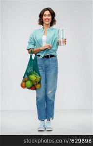 sustainability, eco living and people concept - portrait of smiling young woman with green reusable canvas bag for food shopping and glass bottle of water over grey background. woman with bag for food shopping and glass bottle