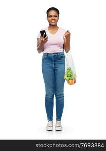 sustainability, food shopping and eco friendly concept - happy smiling african american woman with smartphone holding reusable string bag with fruits and vegetables over white background. woman with smartphone and food in string bag