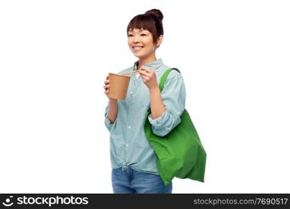 sustainability, food shopping and eco friendly concept - happy smiling asian woman in turquoise shirt and jeans holding reusable green tote bag eating takeaway wok with chopsticks on grey background. asian woman with reusable bag for food and wok