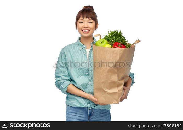 sustainability, food shopping and eco friendly concept - happy smiling asian woman in turquoise shirt and jeans holding paper bag with fruits and vegetables over white background. happy asian woman with food in paper shopping bag