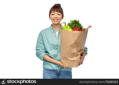 sustainability, food shopping and eco friendly concept - happy smiling asian woman in turquoise shirt and jeans holding paper bag with fruits and vegetables over white background. happy asian woman with food in paper shopping bag