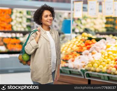 sustainability, food shopping and eco friendly concept - happy smiling woman holding reusable string bag with fruits and vegetables over grocery store background. smiling woman with food in reusable string bag