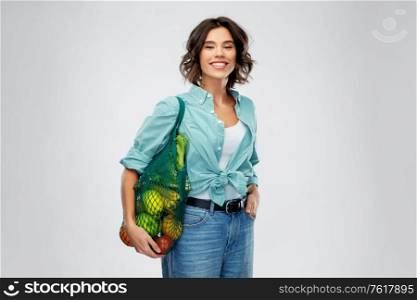sustainability, food shopping and eco friendly concept - happy smiling woman in turquoise shirt and jeans holding reusable net bag with fruits and vegetables on grey background. happy smiling woman with food in reusable net bag