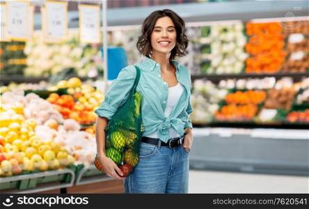 sustainability, food shopping and eco friendly concept - happy smiling woman in turquoise shirt and jeans with reusable net bag with fruits and vegetables over grocery store or supermarket background. happy smiling woman with food in reusable net bag