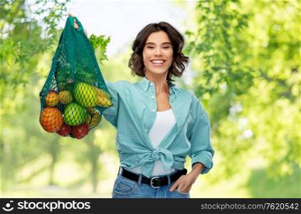 sustainability, food shopping and eco friendly concept - happy smiling woman in turquoise shirt and jeans holding reusable net bag with fruits and vegetables over green natural background. happy smiling woman with food in reusable net bag