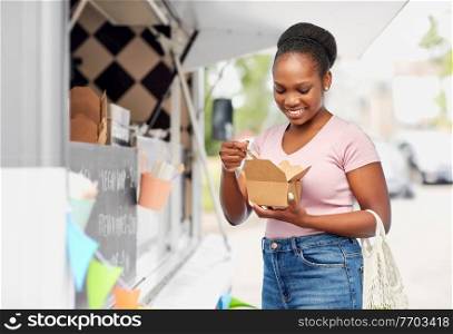 sustainability, shopping and eco friendly concept - happy smiling african american woman with reusable string bag eating takeaway over food truck background. happy woman eating wok over food truck