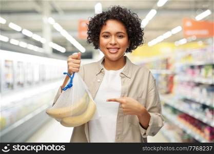 sustainability, shopping and food concept - portrait of happy smiling woman holding reusable string bag with bananas over supermarket or grocery store background. happy woman with bananas in reusable string bag