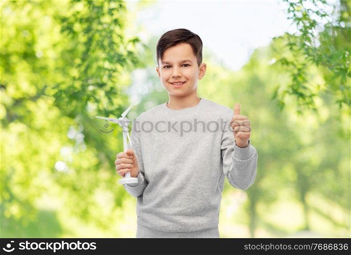 sustainable energy, power and people concept - happy smiling boy with toy wind turbine showing thumbs up over green natural background. smiling boy with toy wind turbine