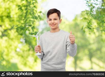 sustainable energy, power and people concept - happy smiling boy with toy wind turbine showing thumbs up over green natural background. smiling boy with toy wind turbine