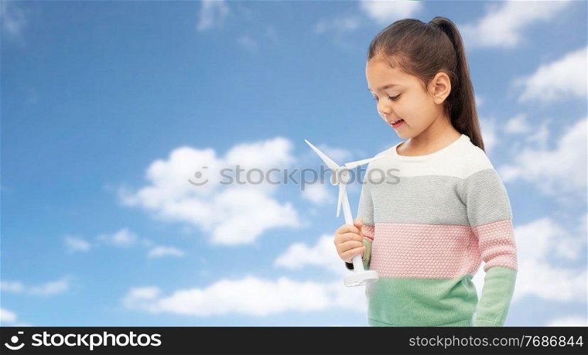 sustainable energy, power and people concept - happy smiling girl with toy wind turbine over blue sky and clouds background. smiling girl with toy wind turbine over blue sky