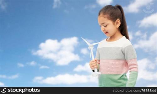 sustainable energy, power and people concept - happy smiling girl with toy wind turbine over blue sky and clouds background. smiling girl with toy wind turbine over blue sky