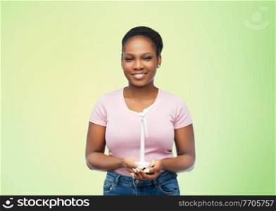 sustainable energy, power and people concept - happy smiling young african american woman with toy wind turbine over green background. happy african american woman with toy wind turbine