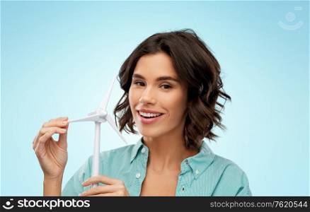 sustainable energy, power and people concept - happy smiling young woman with toy wind turbine over blue background. happy smiling young woman with toy wind turbine