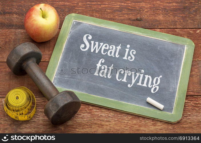 Sweat is fat crying motivational text - slate blackboard sign against weathered red painted barn wood with a dumbbell, apple and tape measure
