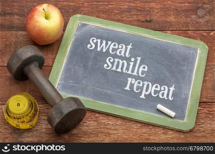 Sweat, smile, repeat - fitness concept - slate blackboard sign against weathered red painted barn wood with a dumbbell, apple and tape measure