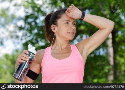 sweaty female jogger holding refillable water bottle