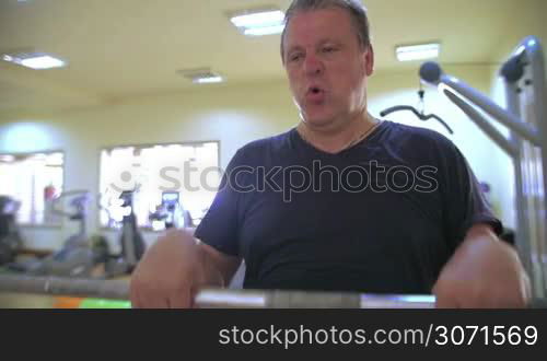 Sweaty mature man lifting barbell the upright position holding it it front of him. Hard work during training