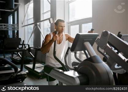 Sweaty sportsman doing cardio exercise on orbitrack training apparatus. Bodybuilder exercising using elliptical machine in modern sport gym. Sweaty sportsman doing cardio exercise on orbitrack training apparatus