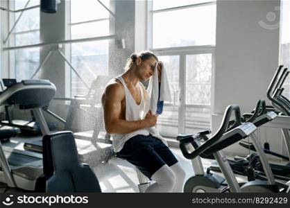 Sweaty tired sportsman wiping wet forehead with towel after hard training on elliptical machine at modern gym sport club. Sweaty tired sportsman wiping wet forehead with towel after hard training