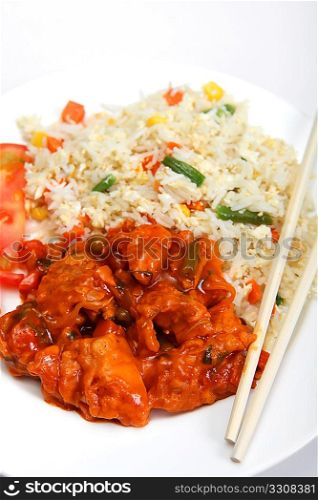 Sweet and sour chicken on a plate with chopsticks, vegetable fried rice and sliced tomato