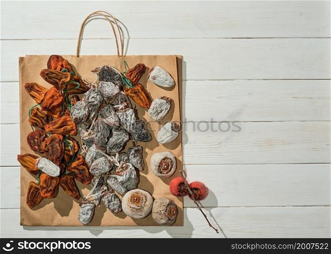 Sweet appetizing healthy dried persimmon on a paper bag. Top view of persimmons bought in the market on a white wooden table with copy space. Traditional Japanese dessert cuisine