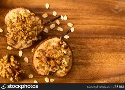 Sweet baked pear halves topped with a crisp crust of oatmeal, sugar and walnut, sprinkled with cinnamon, photographed overhead with natural light (Selective Focus, Focus on the top of the crusts on the pears)