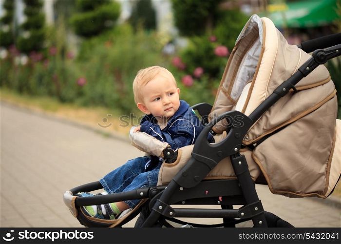 Sweet blonde toddler are sitting in baby carriage outdoor, waiting for mom