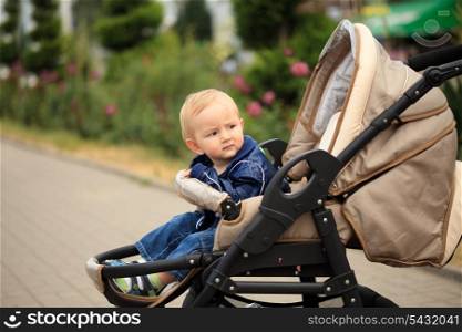 Sweet blonde toddler are sitting in baby carriage outdoor, waiting for mom