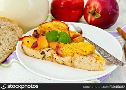 Sweet bread pudding of peaches with milk and eggs in a plate on a linen towel, milk in glass jug, cinnamon on a wooden boards background