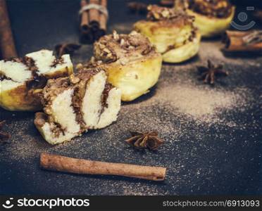 sweet buns with cinnamon and walnuts on a black background sprinkled with powdered cinnamon, vintage toning