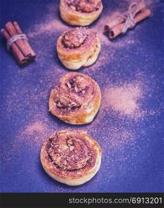 sweet buns with cinnamon and walnuts on a black background sprinkled with powdered cinnamon