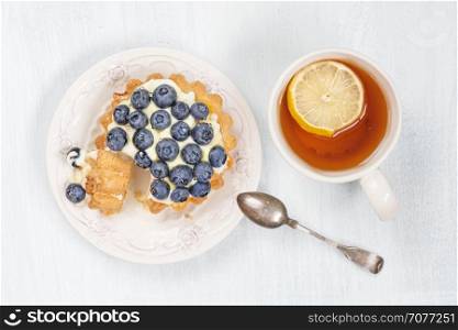 Sweet cake with blueberries, butter cream and syrup, as well as a cup of black tea with a slice of lemon, top view
