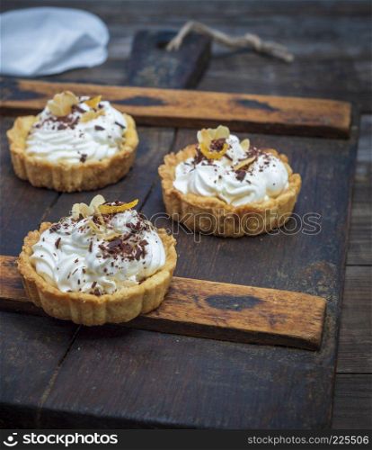sweet cakes with white cream on a brown wooden board, close up
