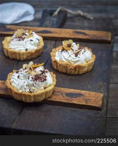 sweet cakes with white cream on a brown wooden board, close up