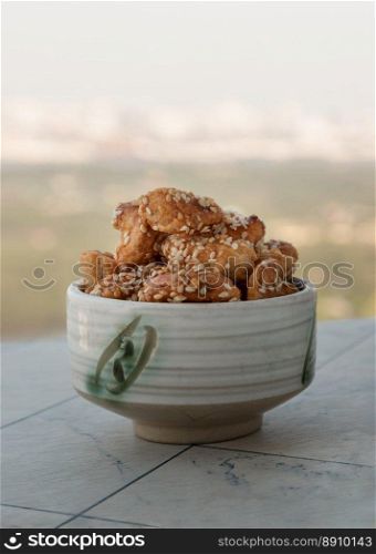 Sweet Cashew Nuts coated with white sesame seeds in the ceramic cup on nature background. Healthy snack, Space for text, Selective Focus.