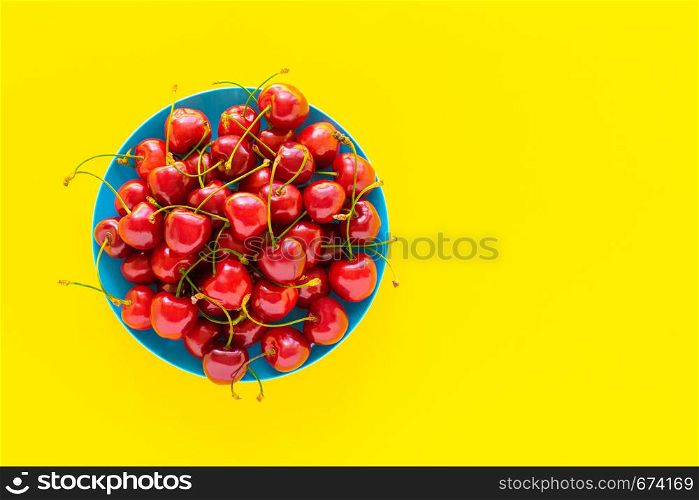 Sweet cherry in a blue plate on a yellow background.