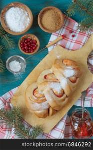 Sweet Christmas pastries with a cowberry jam on an old cutting board surrounded by fir branches, top view