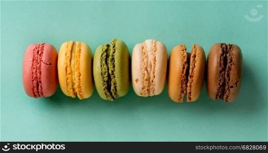 Sweet colorful macarons in a row on a turquoise background