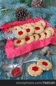 Sweet cookies with jam, fir branches and cones and the bobbin with rough twine on the old wooden table