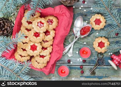 Sweet cookies with jam, fir branches and cones, cranberries, red burning candle and the bobbin with decorative ribbon on the old wooden table