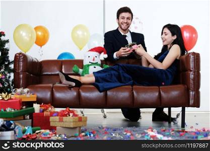 Sweet couple Love happy with surprise gift box girlfriend in christmas time and celebrating new year eve, Valentine day decoration with Christmas tree, colorful balloon and Gift Boxes on brown sofa