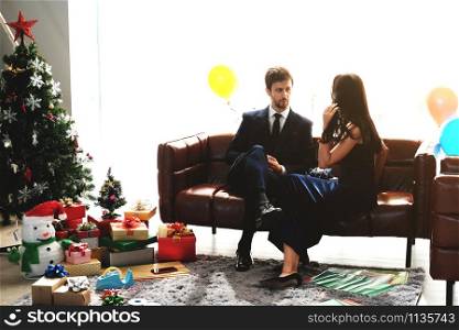 Sweet couple Love smile and spending Romantic christmas time and celebrating new year eve on Brown Sofa decoration with Christmas tree, colorful balloon and Gift Boxes in Living room at home