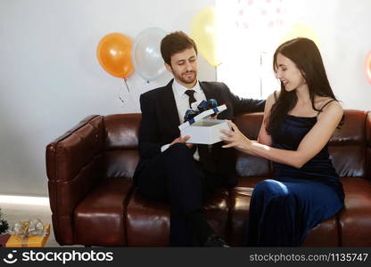 Sweet couple Love smile and spending Romantic christmas time and celebrating new year eve on Brown Sofa decoration with Christmas tree, colorful balloon and Gift Boxes in Living room at home