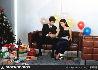 Sweet couple Love smile and spending Romantic christmas time and celebrating new year eve on Brown Sofa decoration with Christmas tree, colorful balloon and Gift Boxes in Living room at home
