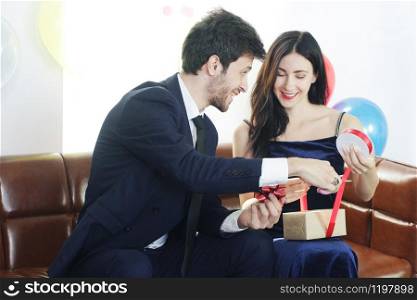 Sweet couple Love smile and spending Romantic christmas time and celebrating new year eve, birthday, and valentine on Brown Sofa decoration with colorful balloon and Gift Boxes in Living room at home