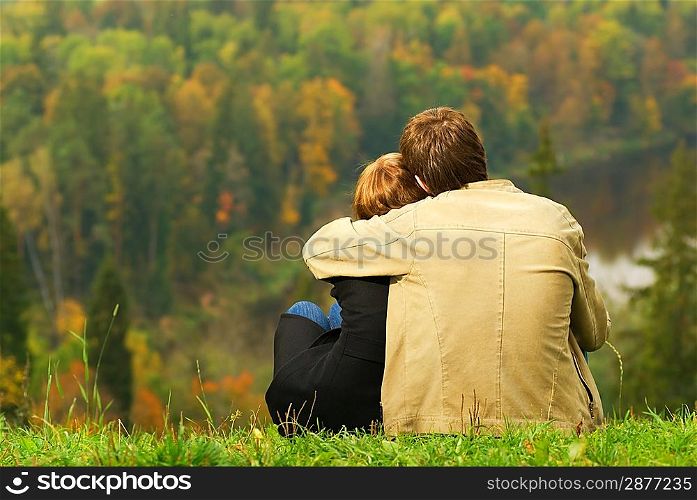 Sweet couple sitting on a hill and looking at the autumn landscape