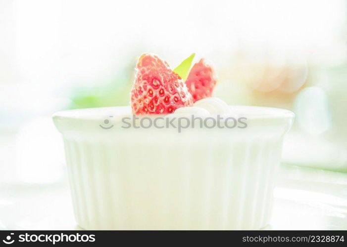 Sweet creme brulee with fresh strawberry on white cup, blurred white background. Close up. Selective focus. High key.