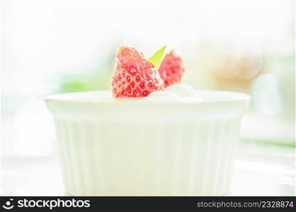 Sweet creme brulee with fresh strawberry on white cup, blurred white background. Close up. Selective focus. High key.