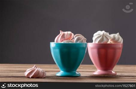 Sweet dessert. Multicolored air meringues in a round vase, on a wooden table.